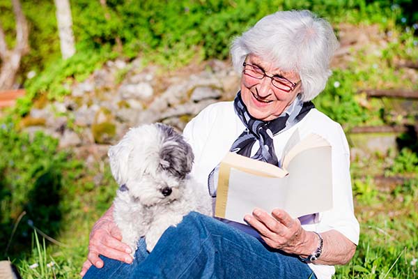 elderly lady reading a book with a pet dog